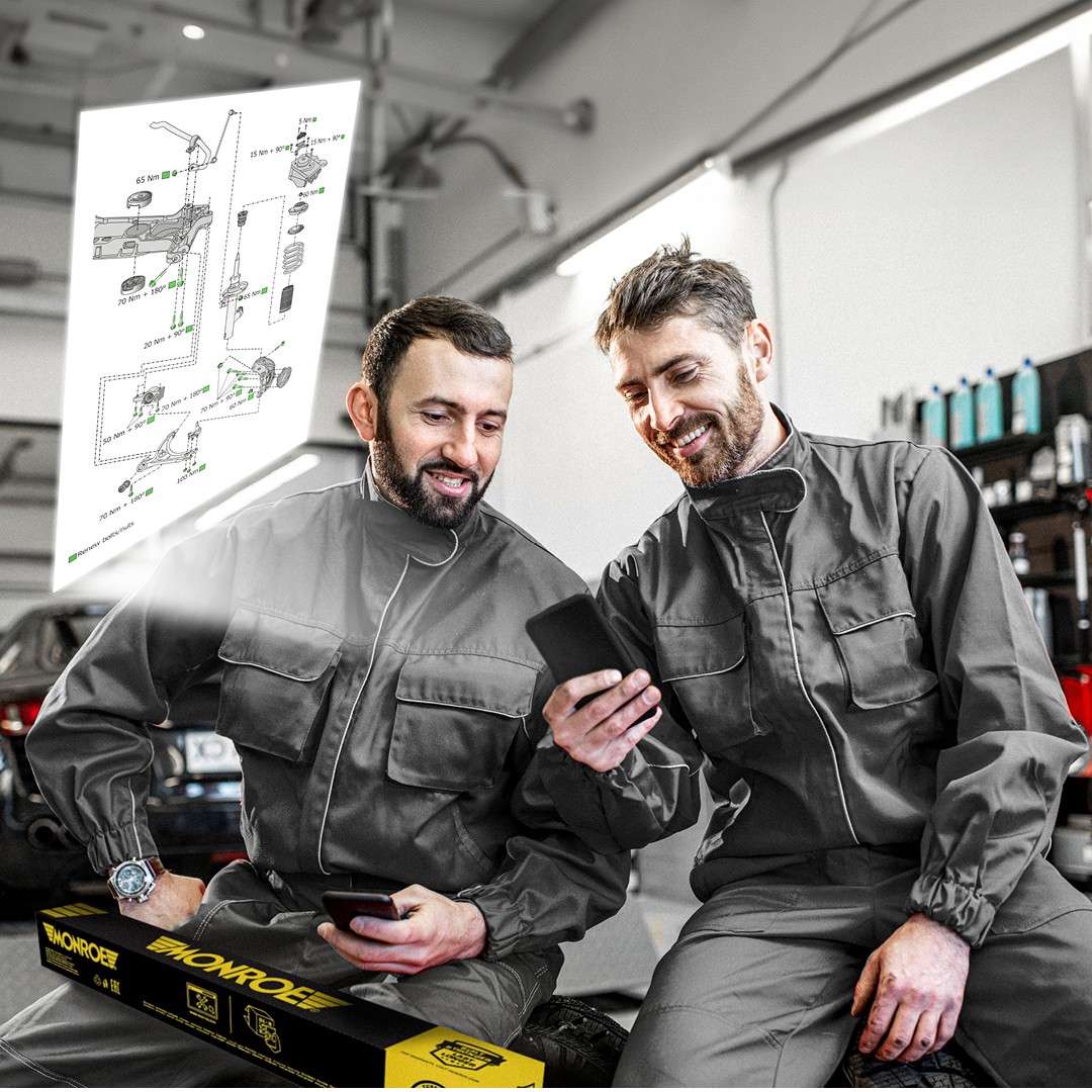 Two automotive mechanics in a workshop examining detailed Monroe technical drawings accessed by scanning a Monroe QR code on the product packaging.